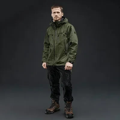 Excursionista con chaqueta impermeable verde, pantalones negros y botas de montaña marrones.